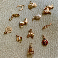 a collection of vintage swedish 18k gold charms or pendants. Included are a collie, a birdcage, a key, a coffee bean, a horseshoe, a moroccan slipper, a heart, a ladybug